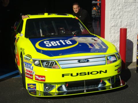 2007 Ford Mustang - A bright yellow Ford Fusion race car, identified by its 'Fusion' text and Ford badge, is parked in a garage area.