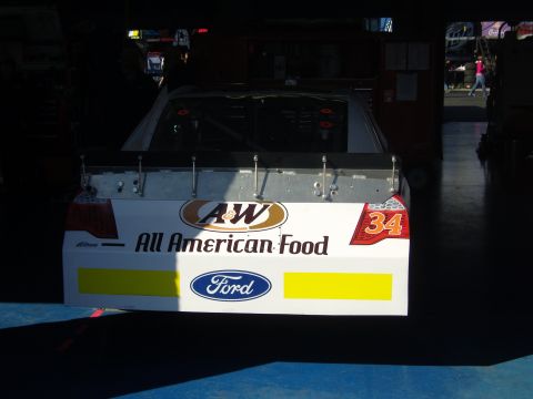 2007 Ford Mustang - A race car with sponsor decals is parked in a garage bay.