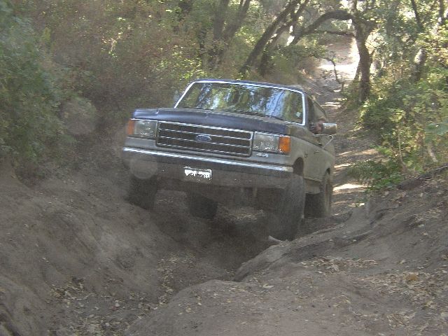 Dark Ford SUV crawling down a rutted dirt trail in the woods, front angle