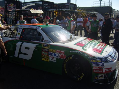 2007 Ford Mustang - A race car with the number 19 and Hunt Brothers Pizza branding is parked at a track with spectators around.