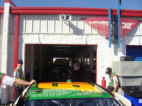 2007 Ford Mustang - A race car is being inspected in a garage bay. Several crew members are present.