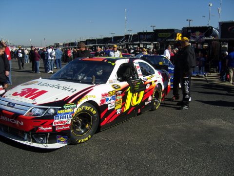 2007 Ford Mustang - A race car with "3M" and "10" logos is parked on the asphalt, with other vehicles and people in the background.
