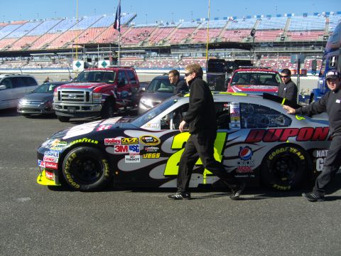 2007 Ford Mustang - A race car with Dupont sponsorship and the number 24 is seen on the track, with other vehicles and grandstands in the background.