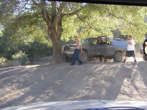 1989 Ford Bronco - People gathered around a dark SUV on a dirt road, with another vehicle in the background.