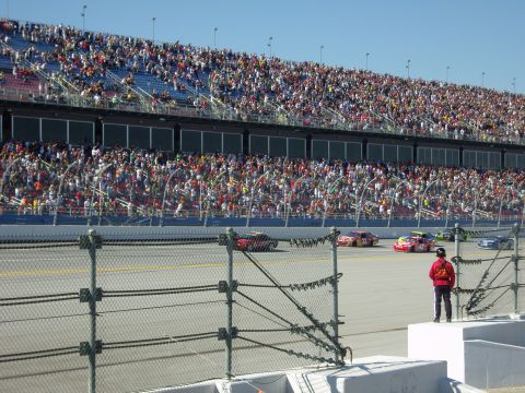 2007 Ford Mustang - A race is underway with multiple cars on the track and spectators filling the grandstands.