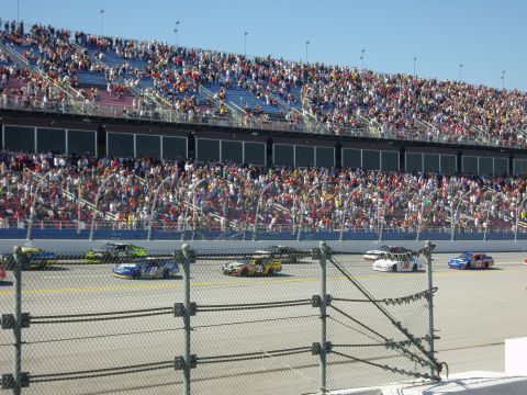 2007 Ford Mustang - A race day scene with multiple stock cars on the track and spectators filling the grandstands.