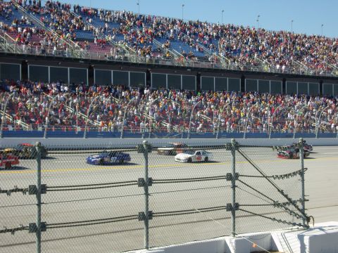 2007 Ford Mustang - Multiple stock cars compete on a race track with a large audience in the stands.