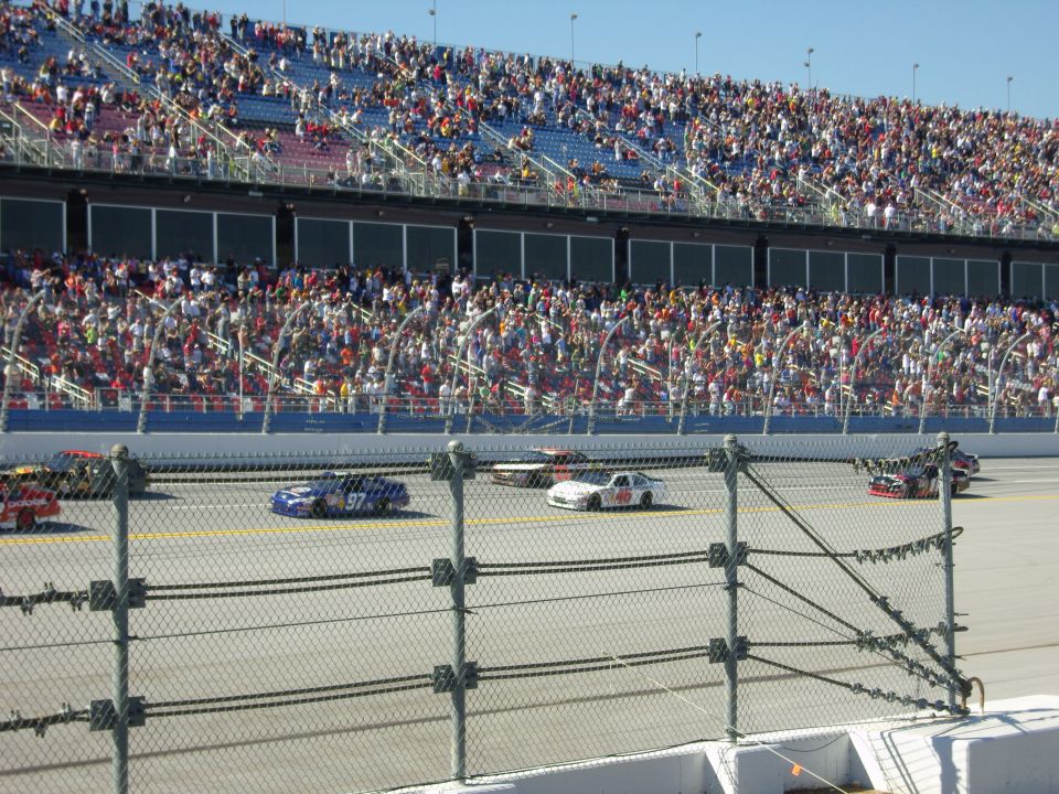 Stock cars race on a track in front of a packed grandstand