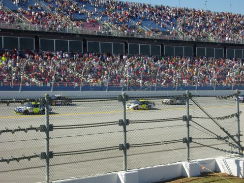 2007 Ford Mustang - Cars race on a track in front of a packed stadium of fans.