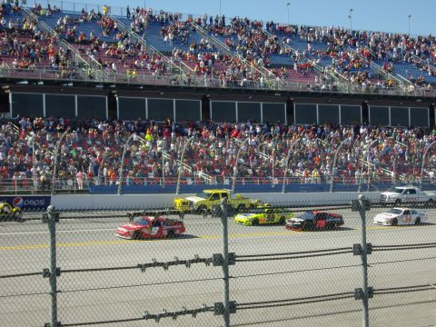 2007 Ford Mustang - Race cars compete on a track with a large crowd watching from the stands.