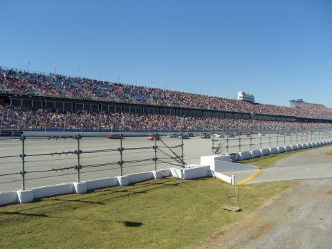 2007 Ford Mustang - A wide view of a race track with multiple cars in action and a large crowd in the stands.
