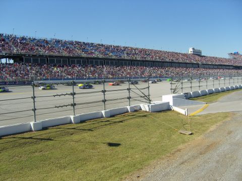 2007 Ford Mustang - Multiple race cars are seen on a track during a race, with a large crowd in the grandstands.