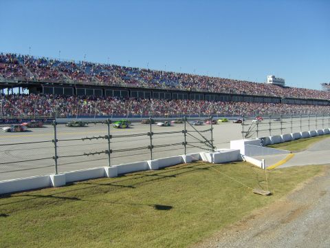 2007 Ford Mustang - Multiple race cars compete on a track in front of a large, crowded grandstand.