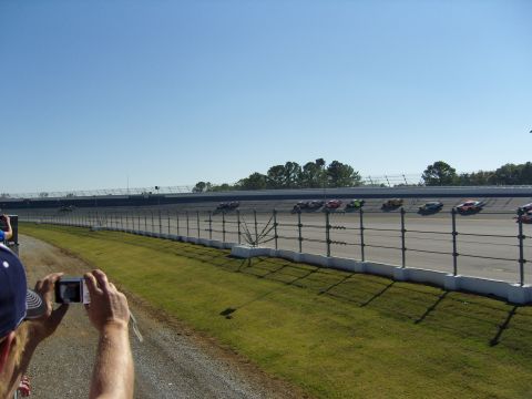 2007 Ford Mustang - Multiple stock cars compete on a race track under a clear blue sky.