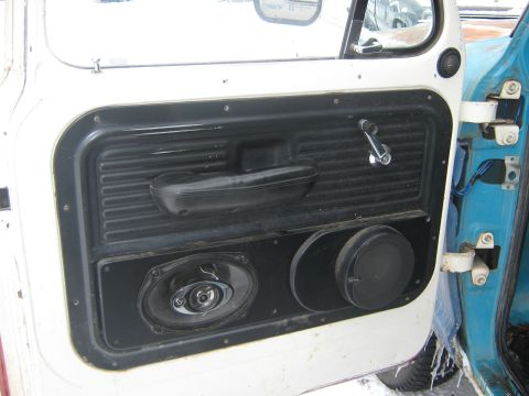 1972 Ford F-250 - Interior view of a white truck door, showing the armrest, window crank, and aftermarket speakers installed in the door panel.