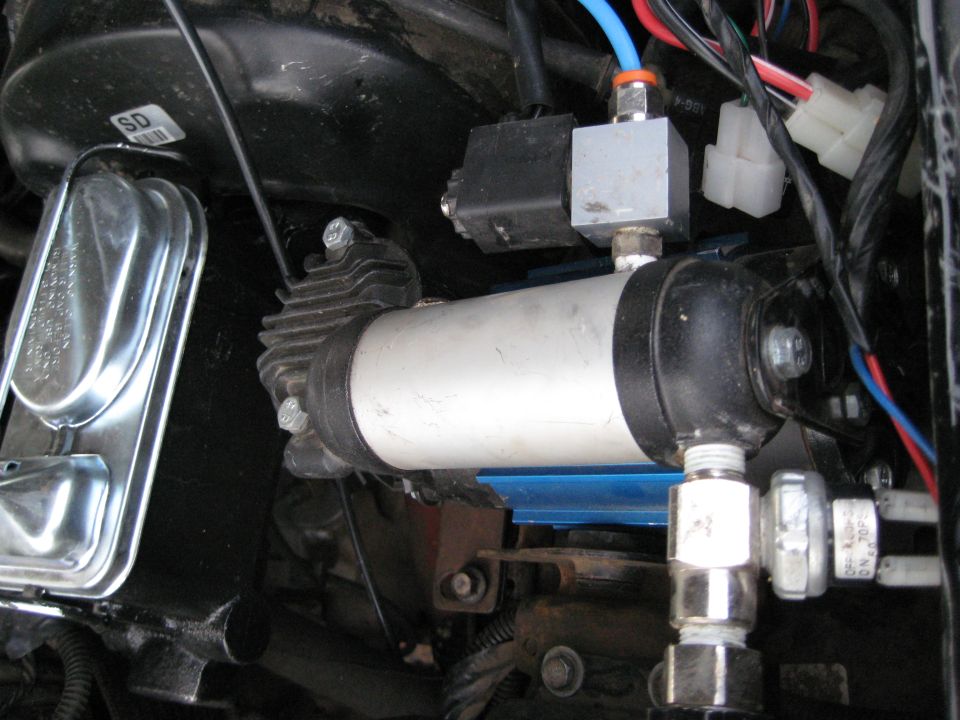 Close-up of an air compressor with a solenoid valve and wiring, mounted in a vehicle