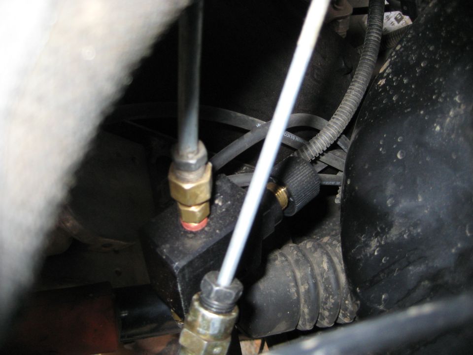 Close-up of brake lines connected to a valve block, with corrugated tubing and wiring visible