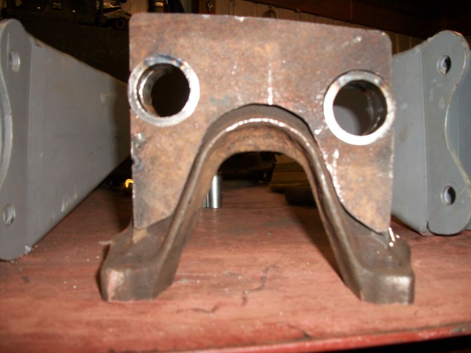 Rusty metal suspension part with two circular holes and a U-shaped bracket, next to a grey metal component