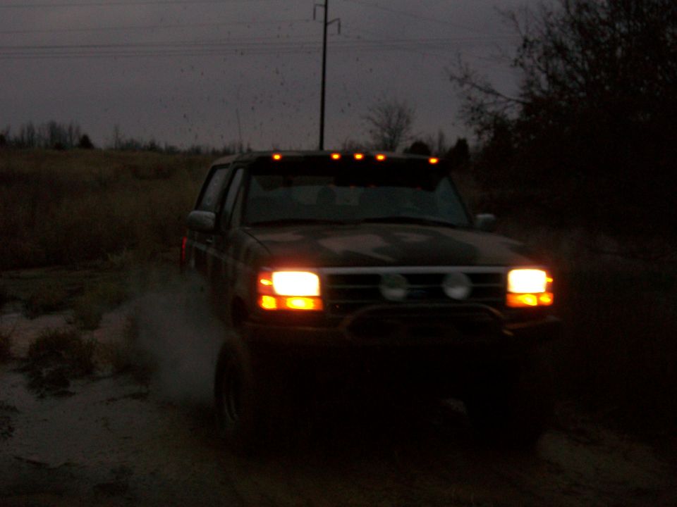 1995 Ford Bronco driving through mud with headlights on