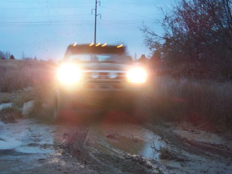1995 Ford Bronco - A truck navigates a muddy path, its headlights cutting through the dim light.
