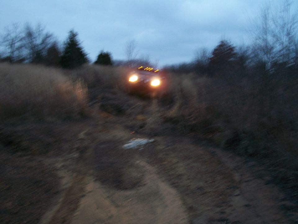 Red SUV driving on dirt road at dusk