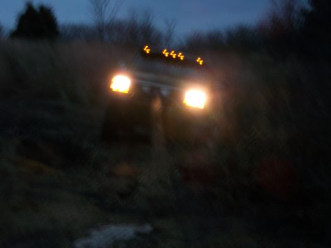1995 Ford Bronco - A 1992 Ford Bronco drives through a dark, grassy area with its lights illuminated.