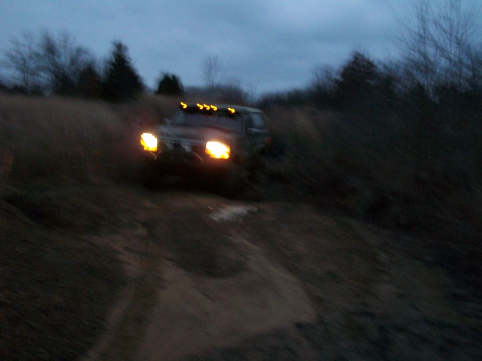 Dark SUV with headlights on driving off-road at dusk