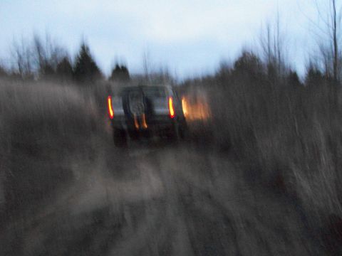 1995 Ford Bronco - SUV driving on a dirt road at dusk with taillights illuminated.
