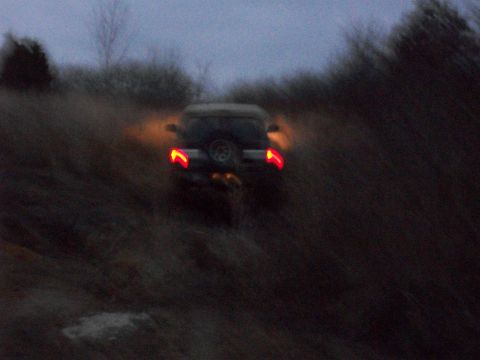 1995 Ford Bronco - An SUV navigates a rough terrain as daylight fades, its taillights illuminating the path ahead.