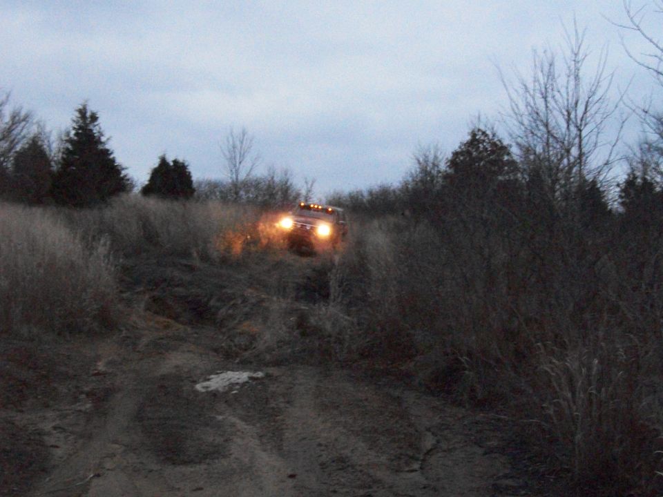 Red Ford Bronco driving on a dirt path through tall grass and trees
