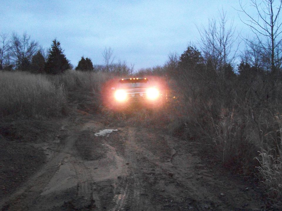 Vehicle with bright headlights on a muddy road at dusk