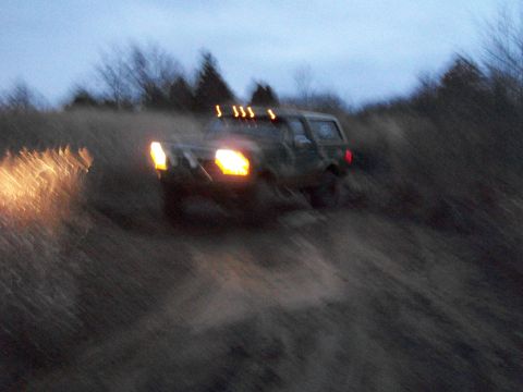 1995 Ford Bronco - 1995 Ford Bronco navigating a grassy hill in low light conditions.