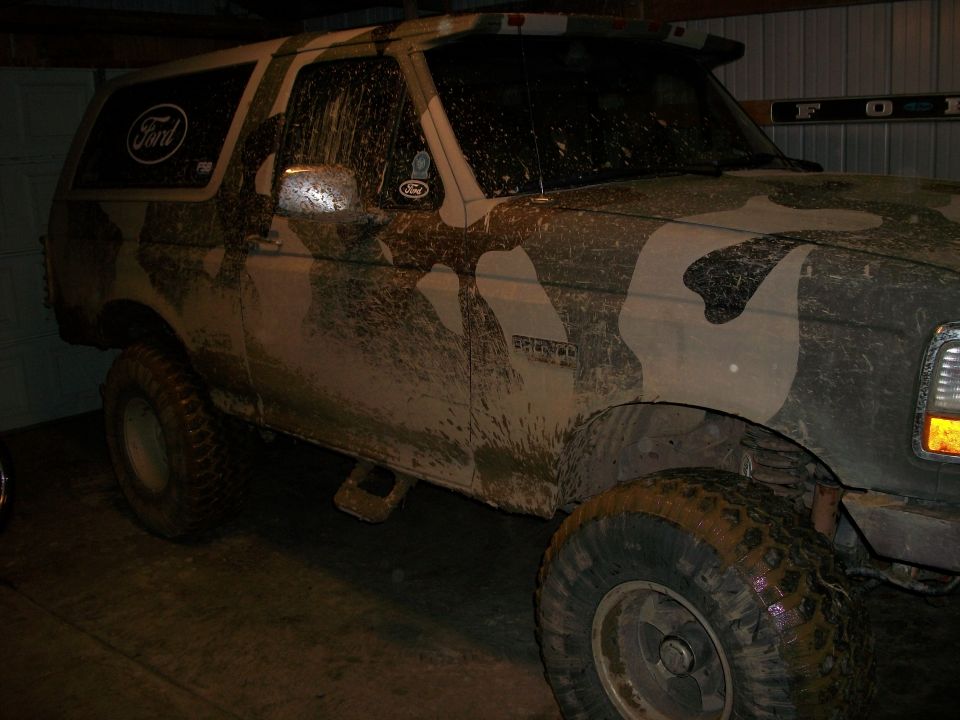 Mud-covered 1995 Ford Bronco with camouflage paint, parked indoors