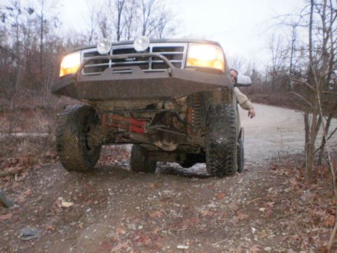 1995 Ford Bronco - This modified Ford Bronco is shown from a low front angle on a dirt road, with a person visible behind the wheel well.
