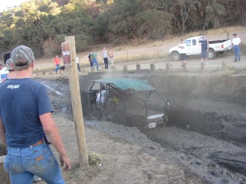 1989 Ford Bronco - An off-road buggy is stuck in a mud pit while a white pickup truck waits nearby.