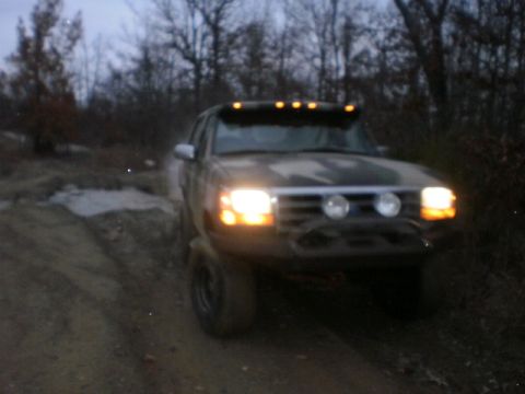 1995 Ford Bronco - 1995 Ford Bronco navigates a dirt road in a wooded area as darkness falls.