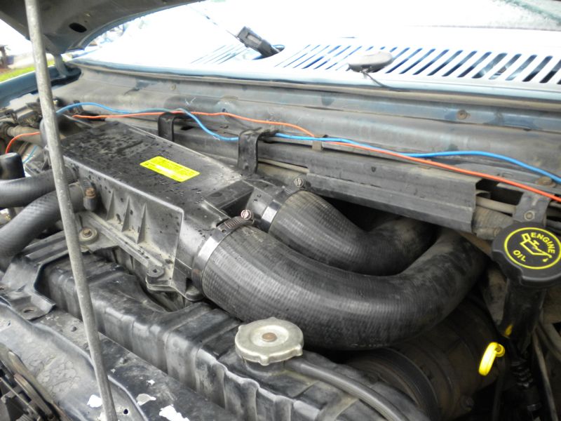 Engine bay with black intake tube, airbox and yellow engine oil cap under open hood