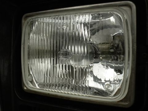 1989 Ford Bronco - Close-up of a vehicle's headlight assembly, showing the Hella logo and DOT certification.