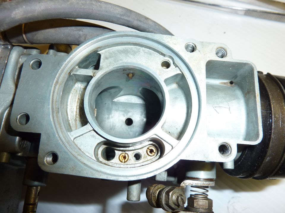 Disassembled aluminum motorcycle carburetor body showing venturi bore and brass jets