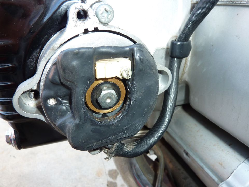 Close-up of a black rubber-sealed round cover with brass ring and center bolt on a motorcycle engine