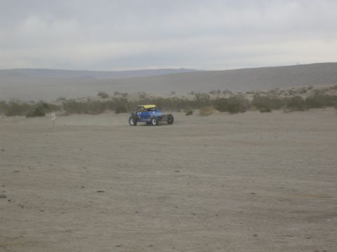 1986 Ford Bronco - Dune buggy navigates sandy terrain under an overcast sky.
