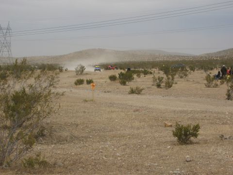 1986 Ford Bronco - Vehicles driving in a dusty desert landscape with hills and power lines overhead.