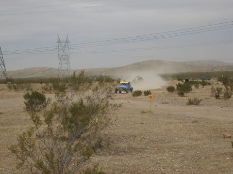 1986 Ford Bronco - Off-road vehicles race through a dusty desert terrain under a cloudy sky, with power lines visible in the background.