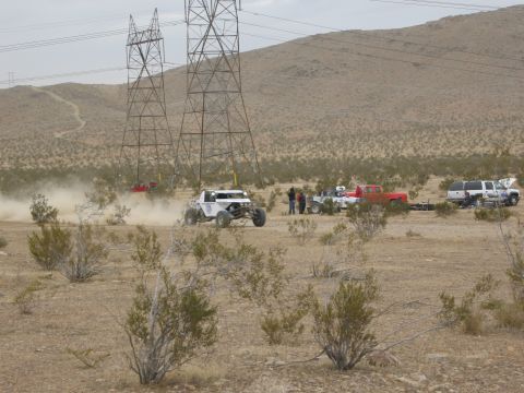1986 Ford Bronco - Several vehicles are gathered in a dusty desert landscape under large power line towers.