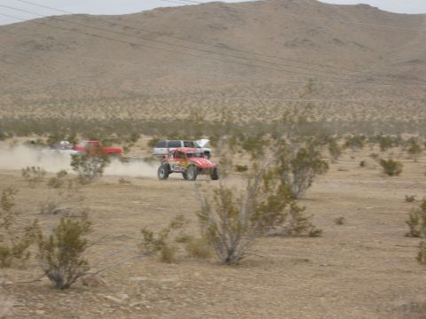 1986 Ford Bronco - Multiple vehicles race across a dusty desert landscape under a cloudy sky.