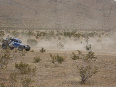 1986 Ford Bronco - A blue off-road buggy kicks up a cloud of dust as it speeds across a dry, desert landscape.