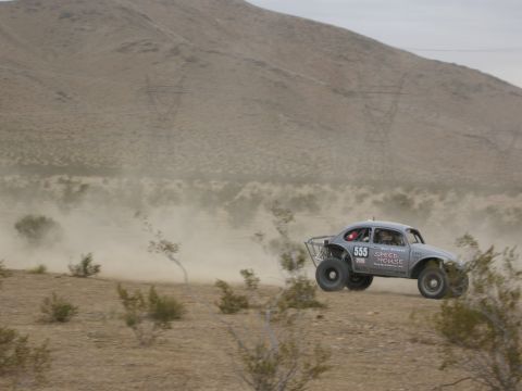 1986 Ford Bronco - Off-road race car jumps over desert terrain, kicking up dust.