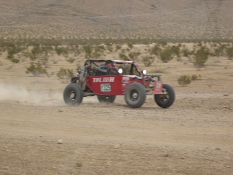 1986 Ford Bronco - A red off-road buggy races across a dusty desert terrain, with sparse vegetation in the background.