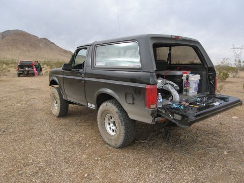 1986 Ford Bronco - A black 1986 Ford Bronco is parked in a desert landscape with its tailgate down, revealing tools and supplies.