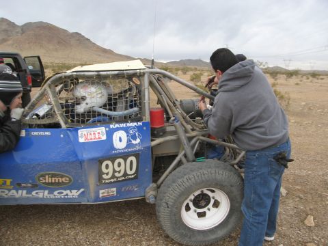 1986 Ford Bronco - Off-road buggy with racing numbers and sponsors visible, being worked on in a desert environment.